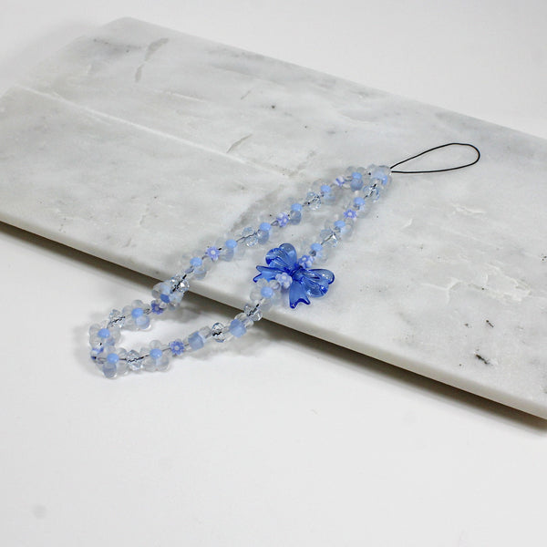 Pastel blue flower phone strap with bow laid on a marble surface, perfect for women and girls.