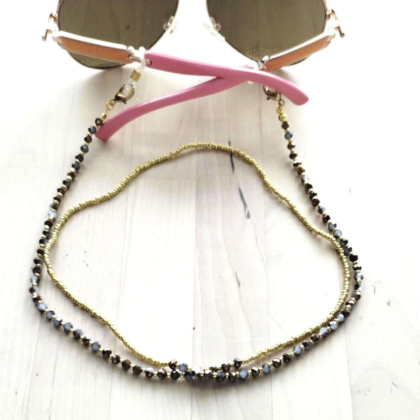 Handmade beaded eyeglass chain featuring sparkling glass beads and sunglasses resting on a wooden surface.