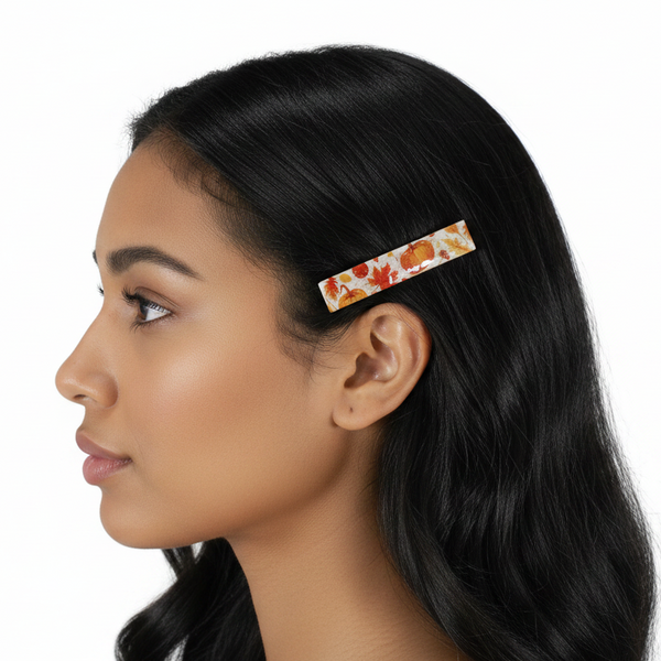 A side-profile view of awoman with long black hair wearing a slim hair clip decorated with an autumn leaf and pumpkin pattern on a white background.
