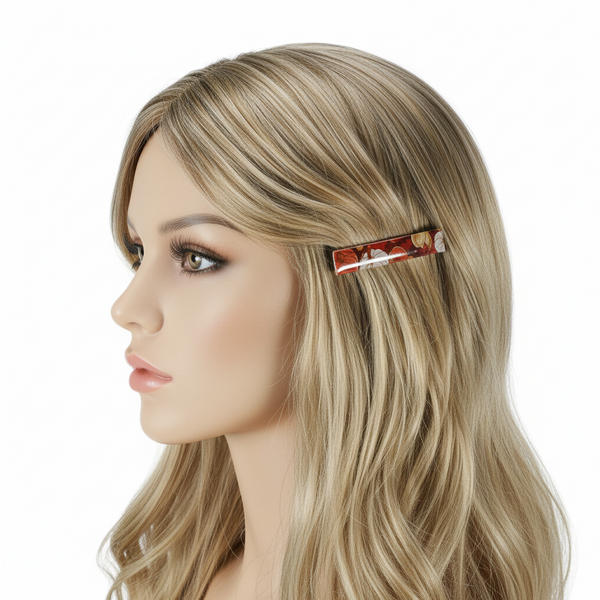 A side-profile view of a mannequin head with long black hair and a small rectangular hair clip in the hair. The clip has a red-orange background with a floral pattern.