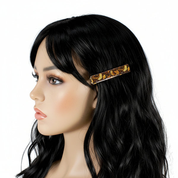 A side-profile view of a mannequin head with long black hair, wearing a tortoiseshell hair clip on the side of the head, against a plain white background.