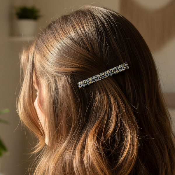 A close-up lifestyle shot of a woman with long, wavy light brown hair wearing a slim, rectangular barrette hair clip with a colorful floral pattern.