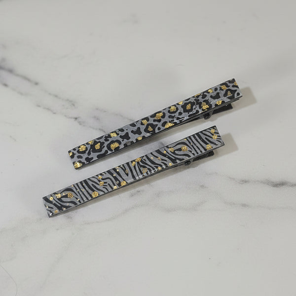 Two slim rectangular hair clips with animal print patterns, one leopard print and one zebra print