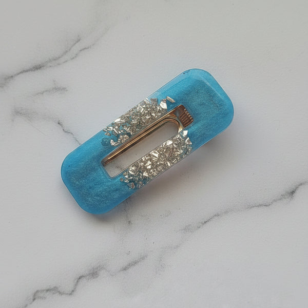 A turquoise blue hair claw clip decorated with silver rhinestones and a small gold bow accent, shown on a plain light gray background.