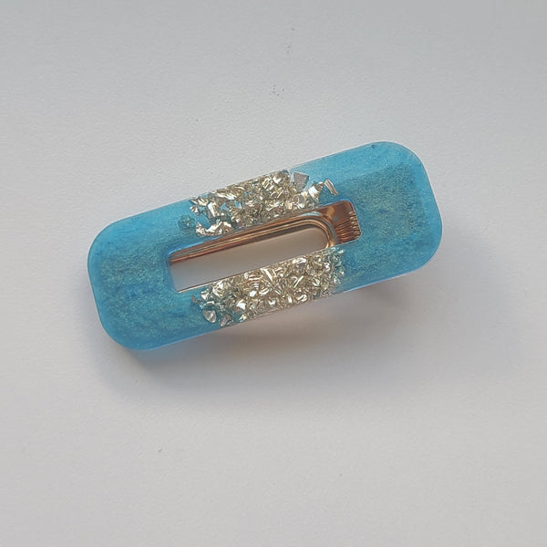 A turquoise blue hair claw clip embellished with two rows of sparkling clear rhinestones on a plain light gray background.