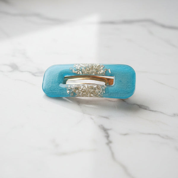 A turquoise blue hair claw clip embellished with two rows of sparkling clear rhinestones on a plain light gray background.