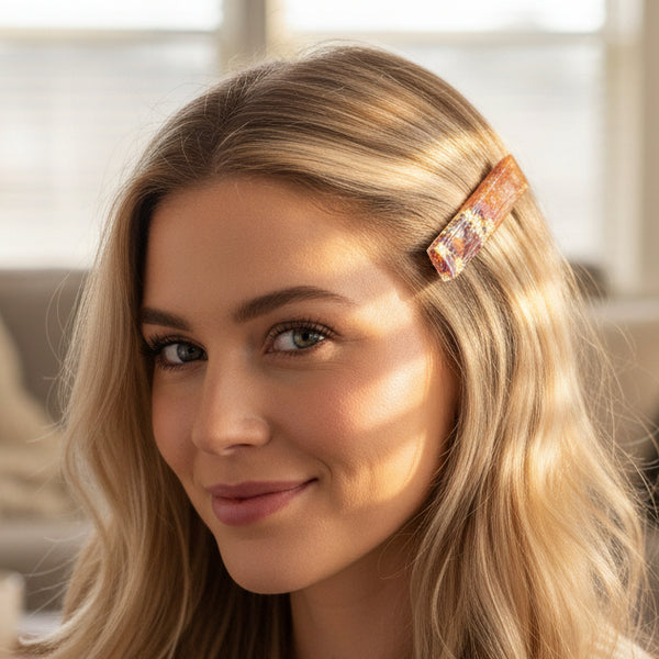 A rectangular clear resin hair clip with a gradient from orange to pink, filled with glitter and decorated with colorful metallic maple leaf flakes